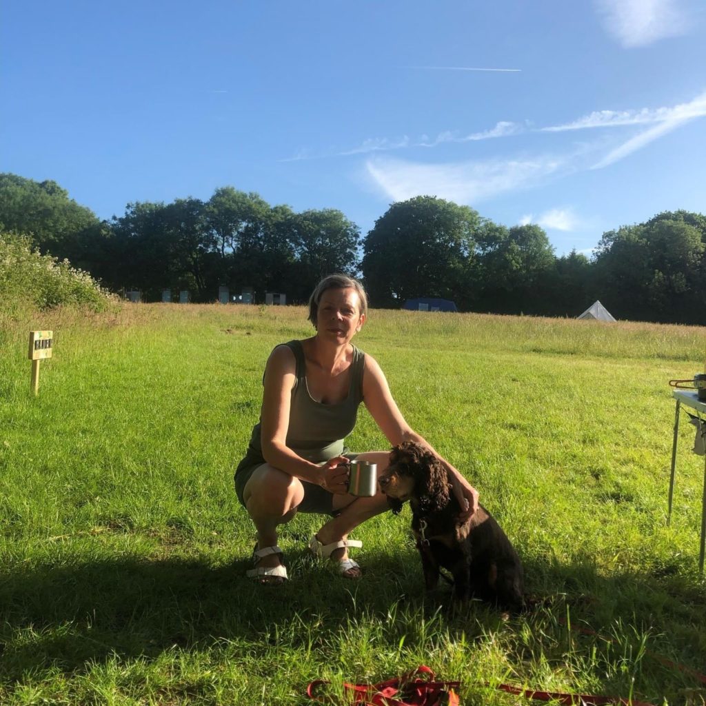 Happy woman and dog with coffee in a green field with blue sky