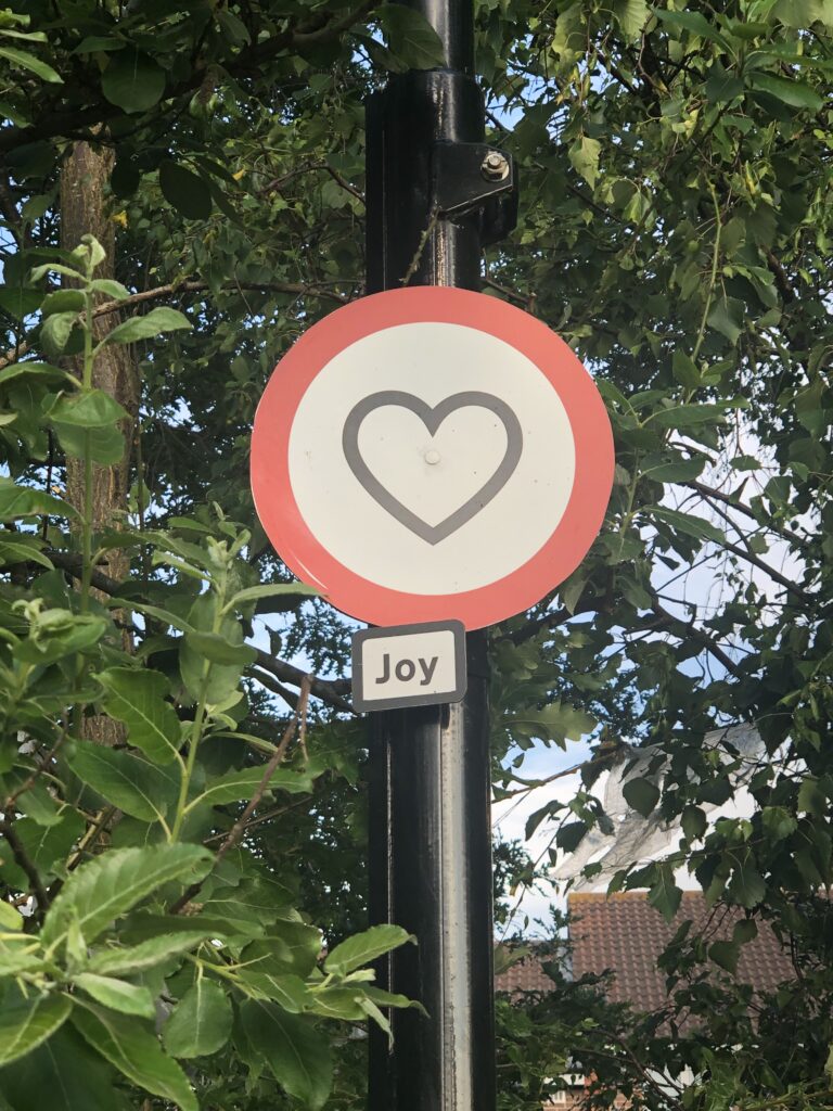 Circular, guerilla road sign of a heart with the word "Joy' written underneath. In my local neighbourhood of Sydenham, London