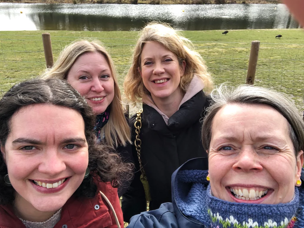4 women in a group outdoors, lake in background, selfie
