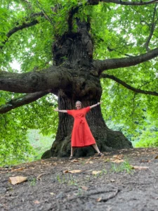 Smiling woman, arms outstretched in front of a huge and wide oak tree